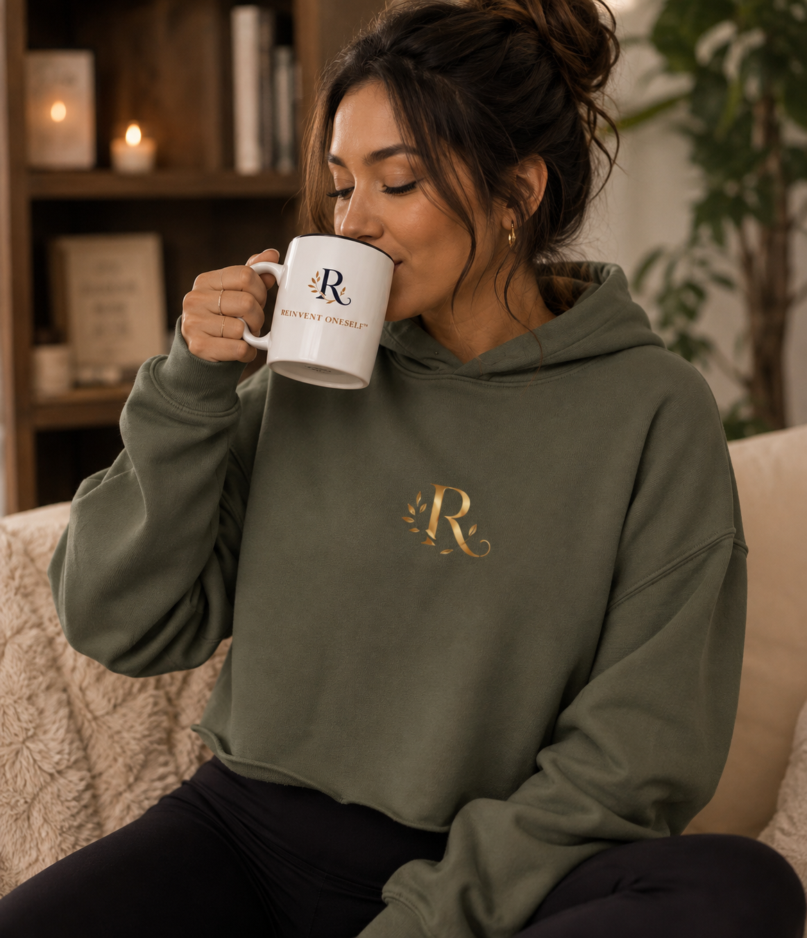 Woman in the olive cropped hoodie holding the Reinvent Oneself ceramic mug